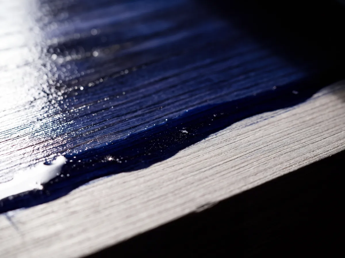 Deep navy coating flowing across a raw wood surface