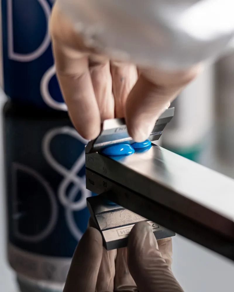 Gloved hands testing a coated sample, with a DAAS & Chemicals can in the background