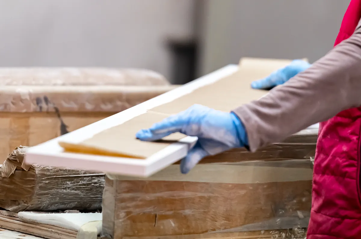 Gloved hands handling a coated wood panel in a finishing department