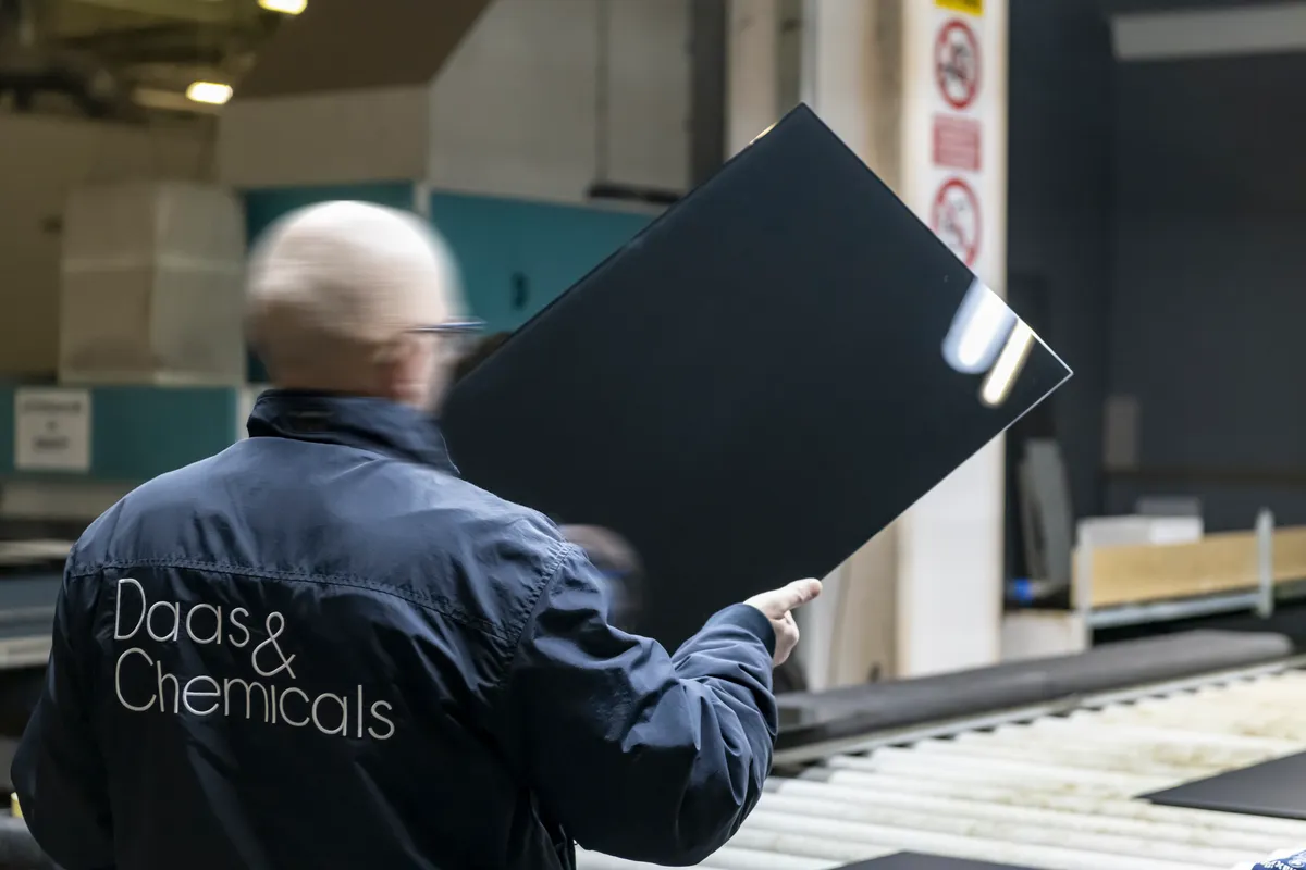 DAAS & Chemicals operator holding a coated glass panel on the production line